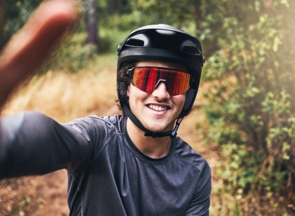 man-taking-selfie-while-cycling-nature-trail-wearing-helmet-sunglasses-portrait-cyclist-bicycle-ride-through-park-forest-taking-picture-smiling-wearing-safety-gear