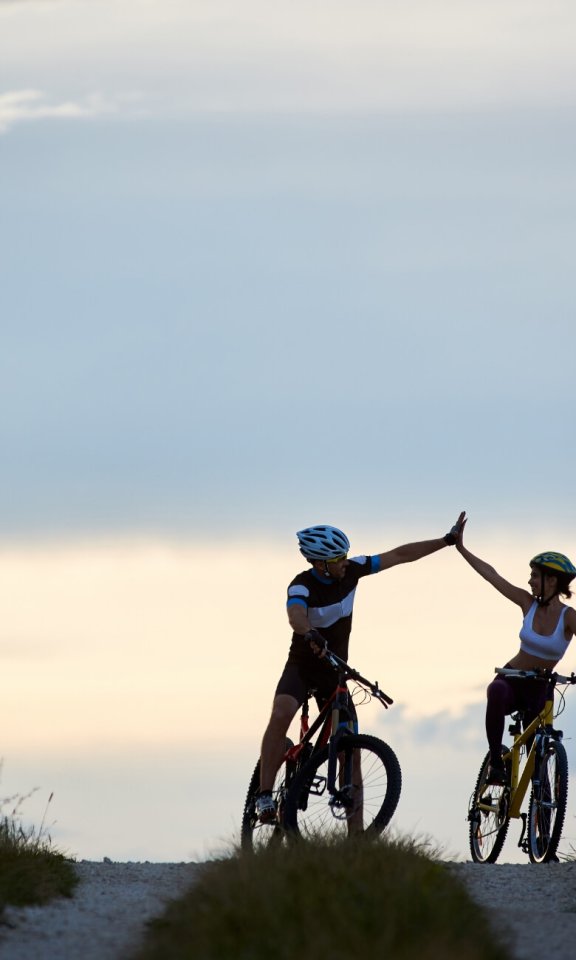 sporty-woman-man-riding-bicycles-having-fun-outside-silhouettes-sportsmen-highing-five-posing-road-sunset-time-non-urban-scene